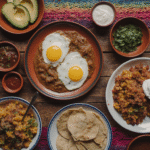 Colorful Mexican breakfast spread featuring huevos rancheros, chilaquiles, tortillas and fresh salsa on wooden table