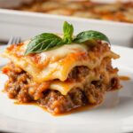 A portion of perfectly baked homemade lasagna with bubbling cheese and rich layers, served on a plate with fresh basil garnish.