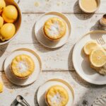 A vibrant assortment of homemade lemon desserts including a glazed loaf, meringue pie, and cookies on a rustic table.