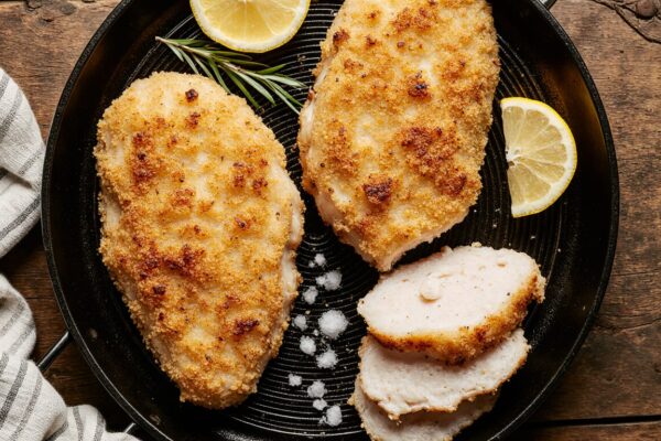 Golden-brown, perfectly fried chicken cutlets on a wire rack with lemon wedges and fresh herbs