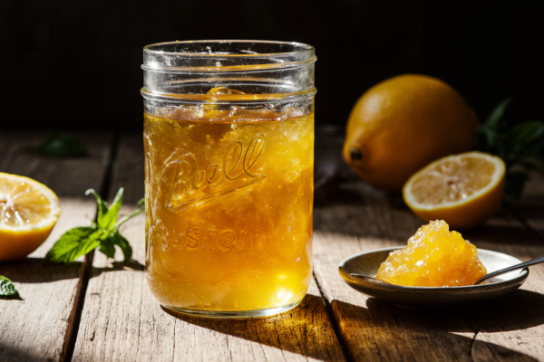 A jar of vibrant homemade lemon jam with visible zest, photographed in warm natural light to showcase its glossy, inviting texture.