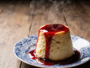 A perfect, golden Steamed Sponge Pudding on a plate, glistening with sticky syrup and releasing steam.