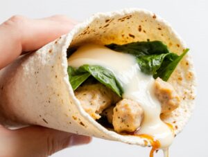 Close-up of assembling chicken wraps with garlic and cheese, showing the creamy garlic chicken and melted mozzarella being wrapped in a warm tortilla.