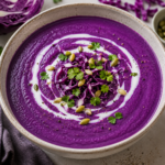 Creamy purple cabbage soup made with red cabbage and coconut milk, garnished with fresh herbs, shredded cabbage, and pumpkin seeds.